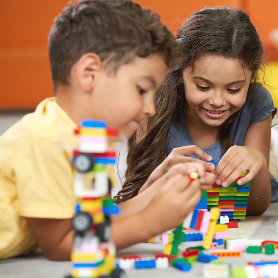 Two children playing with colorful building blocks on the floor.