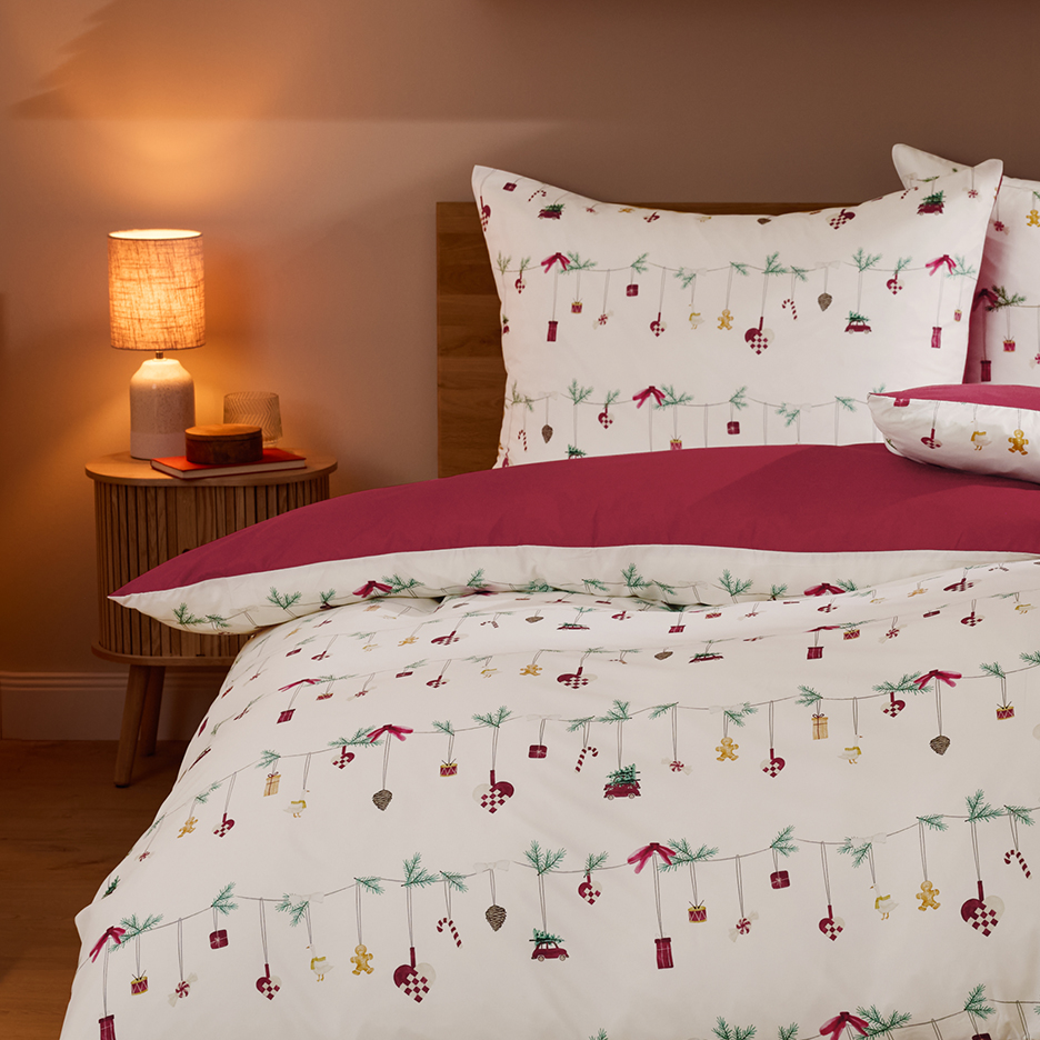 Christmas-themed bedding with red duvet cover in a bedroom with a bedside table and lamp.