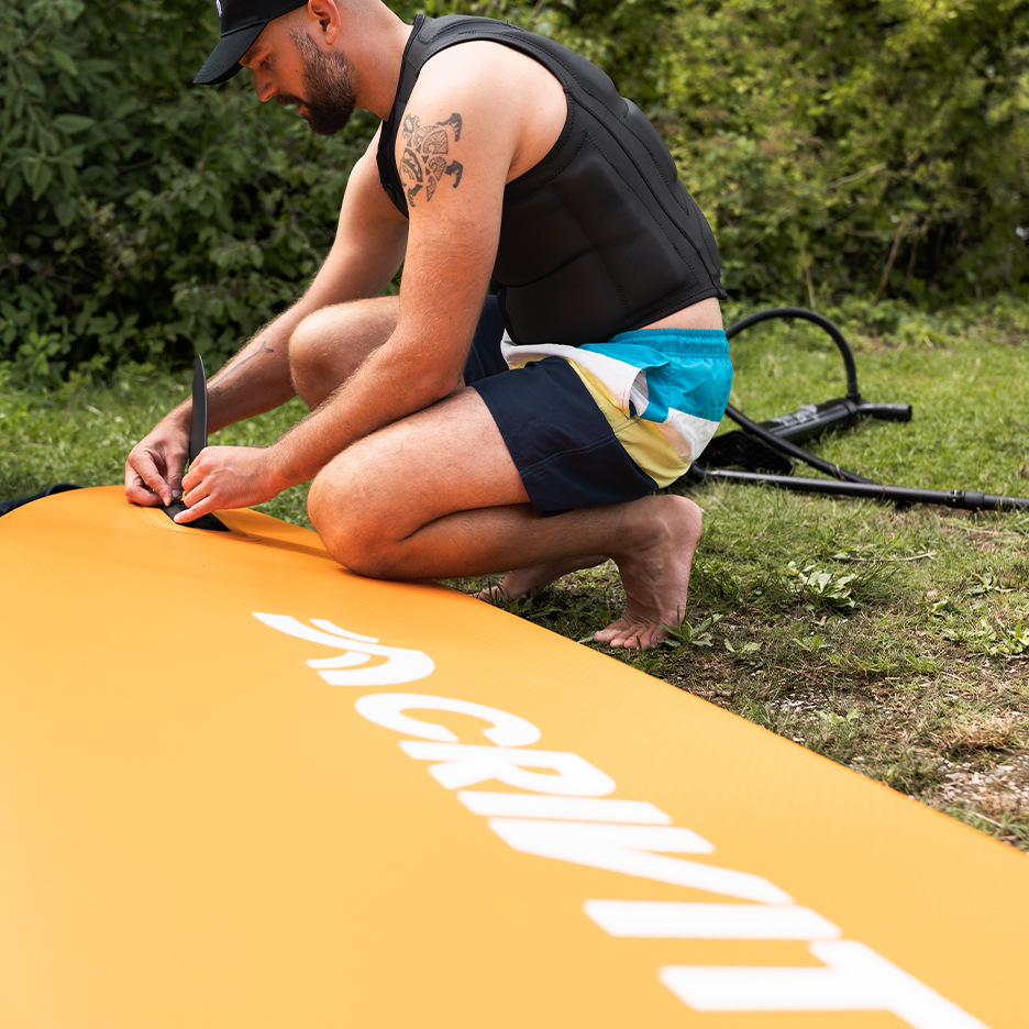 Man assembling an orange paddleboard, wearing a life vest and swim shorts.