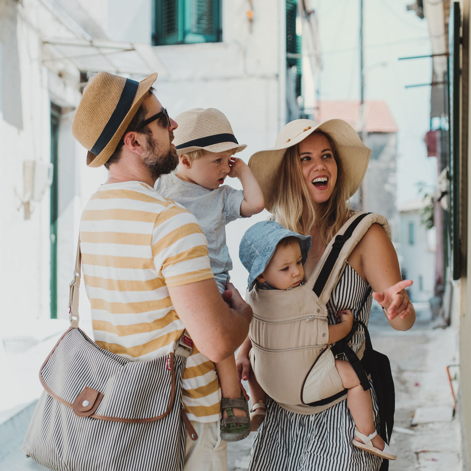 Family with two toddlers, striped bag and baby carrier.