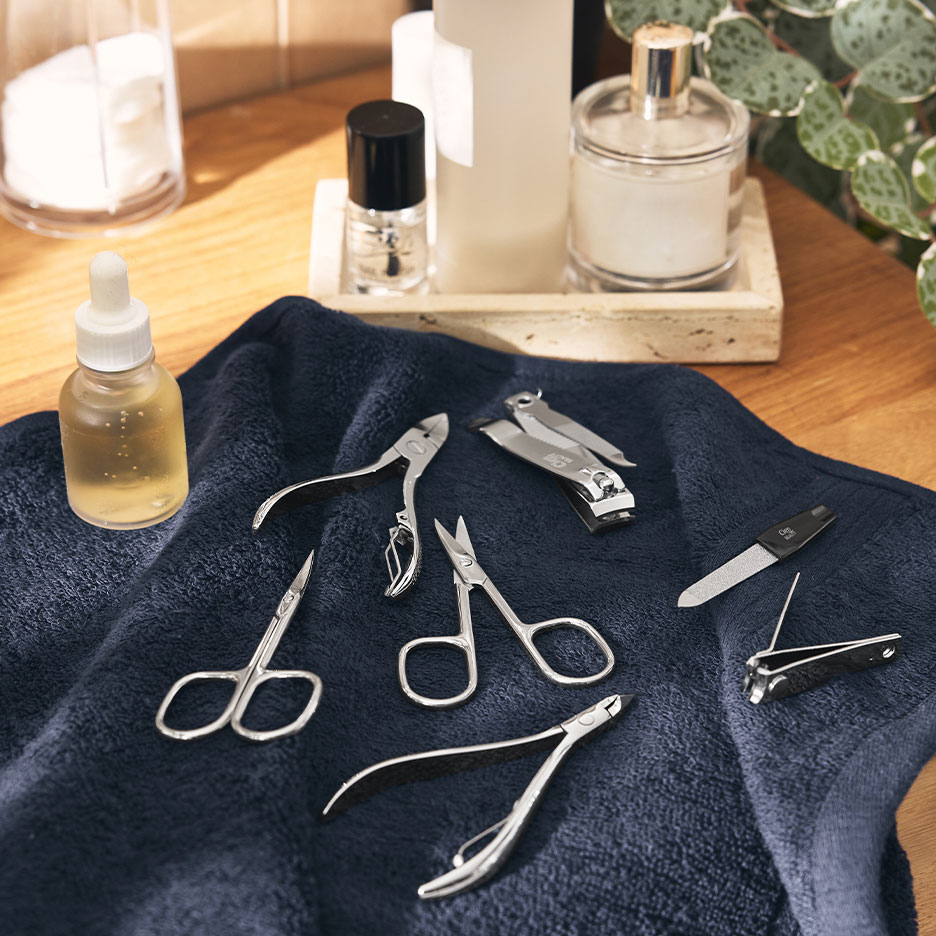 Manicure set with nail clippers, scissors, and files on a dark blue towel.