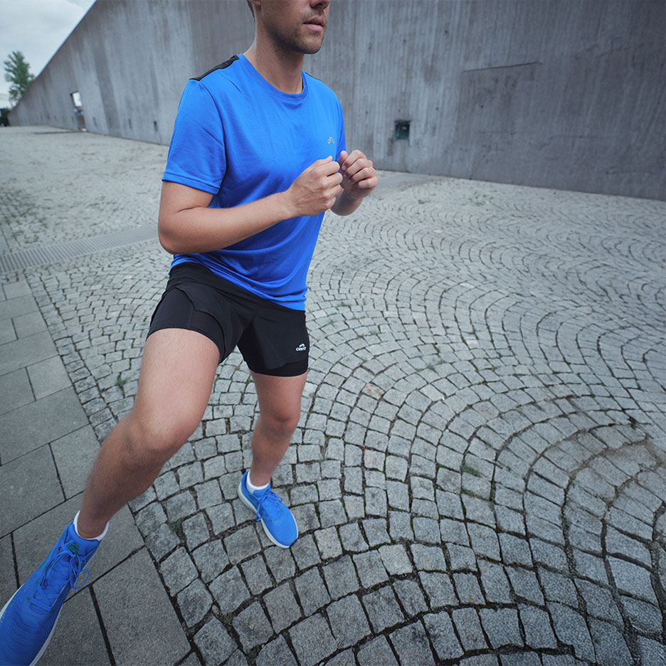 Man in blue t-shirt and black running shorts jogging on cobblestones.