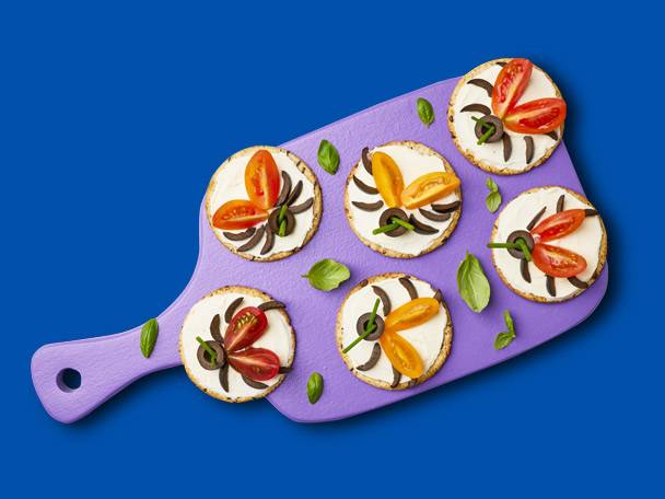 Crackers with cheese, tomatoes, and olives, shaped like spiders.