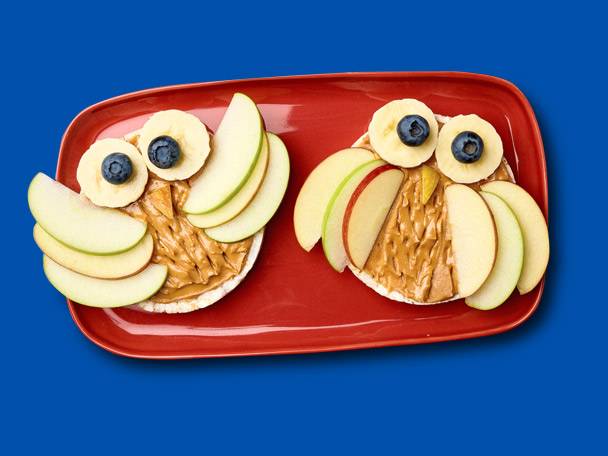 Rice cakes with peanut butter, fruit, and blueberries, shaped like owls.