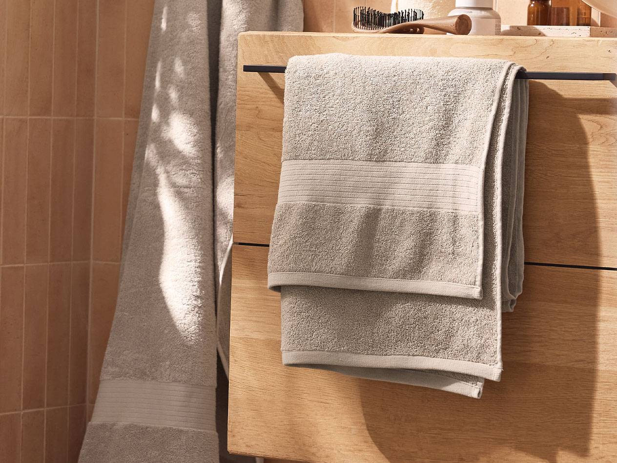 Light grey towels hanging on a wooden cabinet in a bathroom.