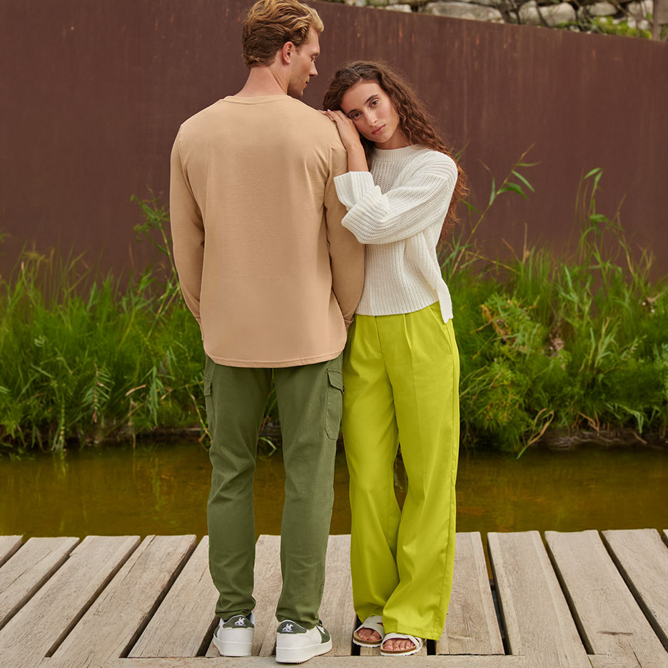 Couple in casual wear: man in beige long-sleeve and olive cargo pants, woman in white sweater and lime trousers.