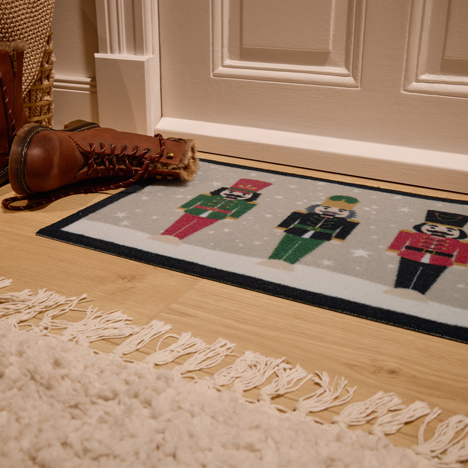 Christmas nutcracker doormat and brown boots by a white door.