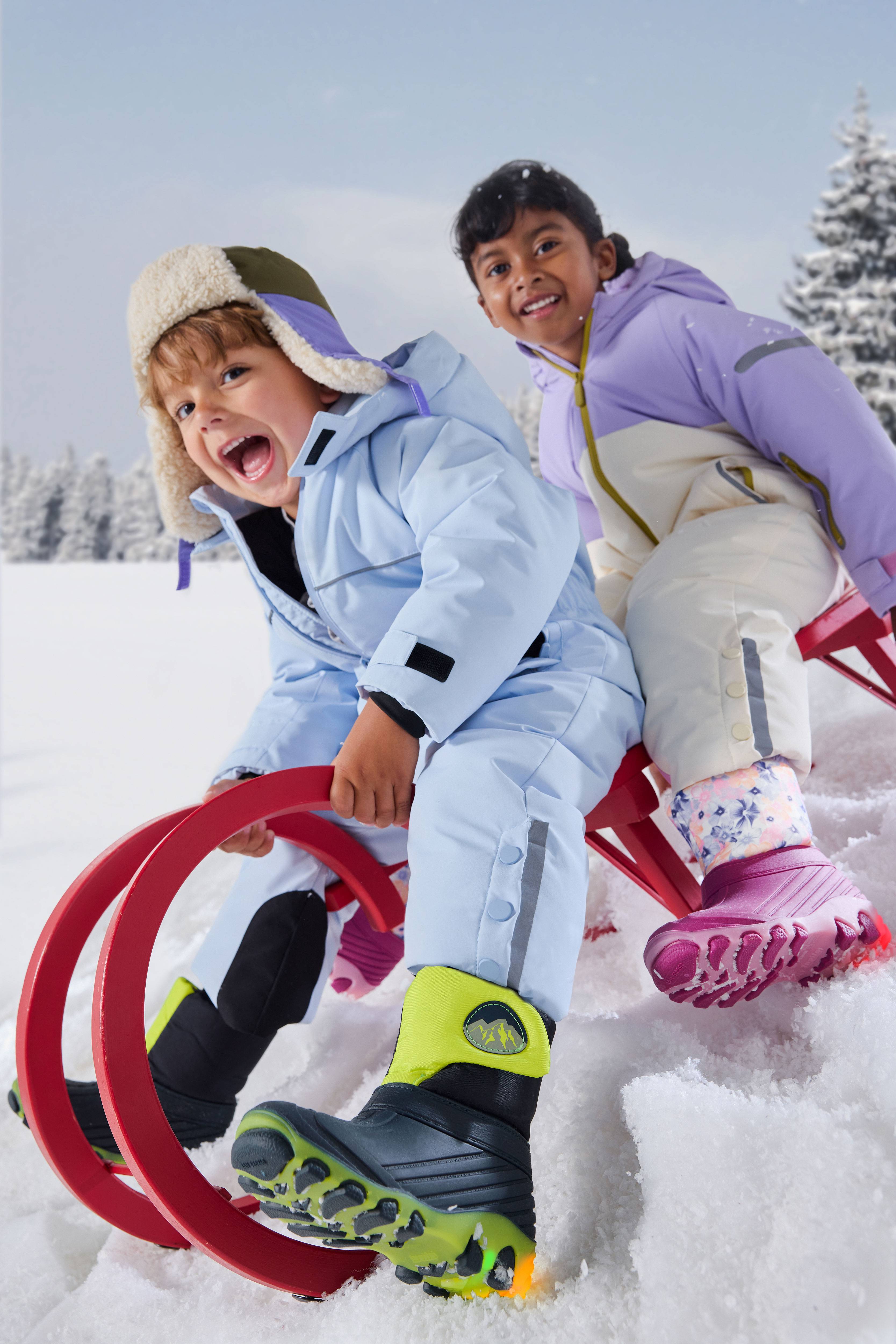 Happy children in snowsuits and winter boots sledding in the snow.