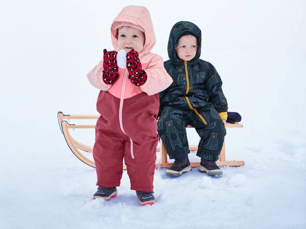 Two children in winter jumpsuits and mittens on a sled in the snow.