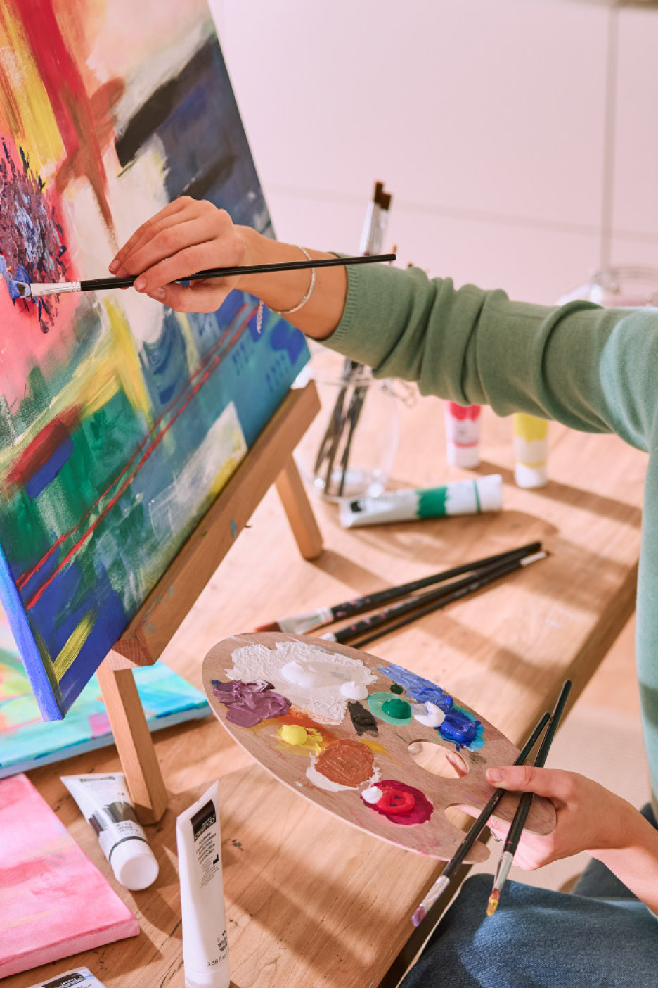 Person painting on a canvas with a brush and a palette of colorful paints.