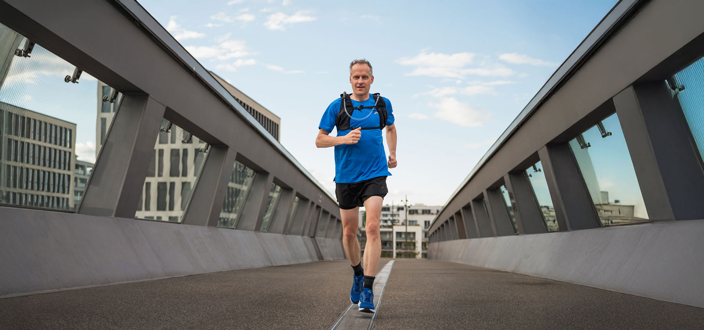 Runner with hydration pack jogging on a modern bridge.