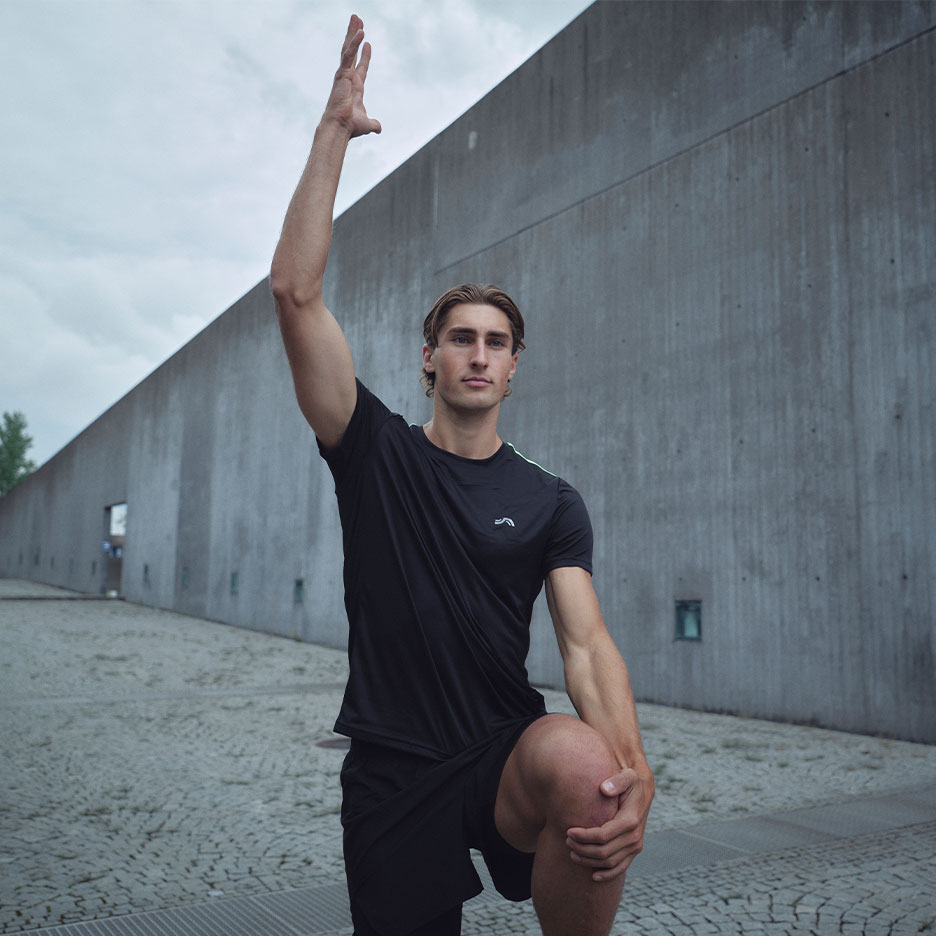 Man in black workout T-shirt and shorts stretching outdoors.