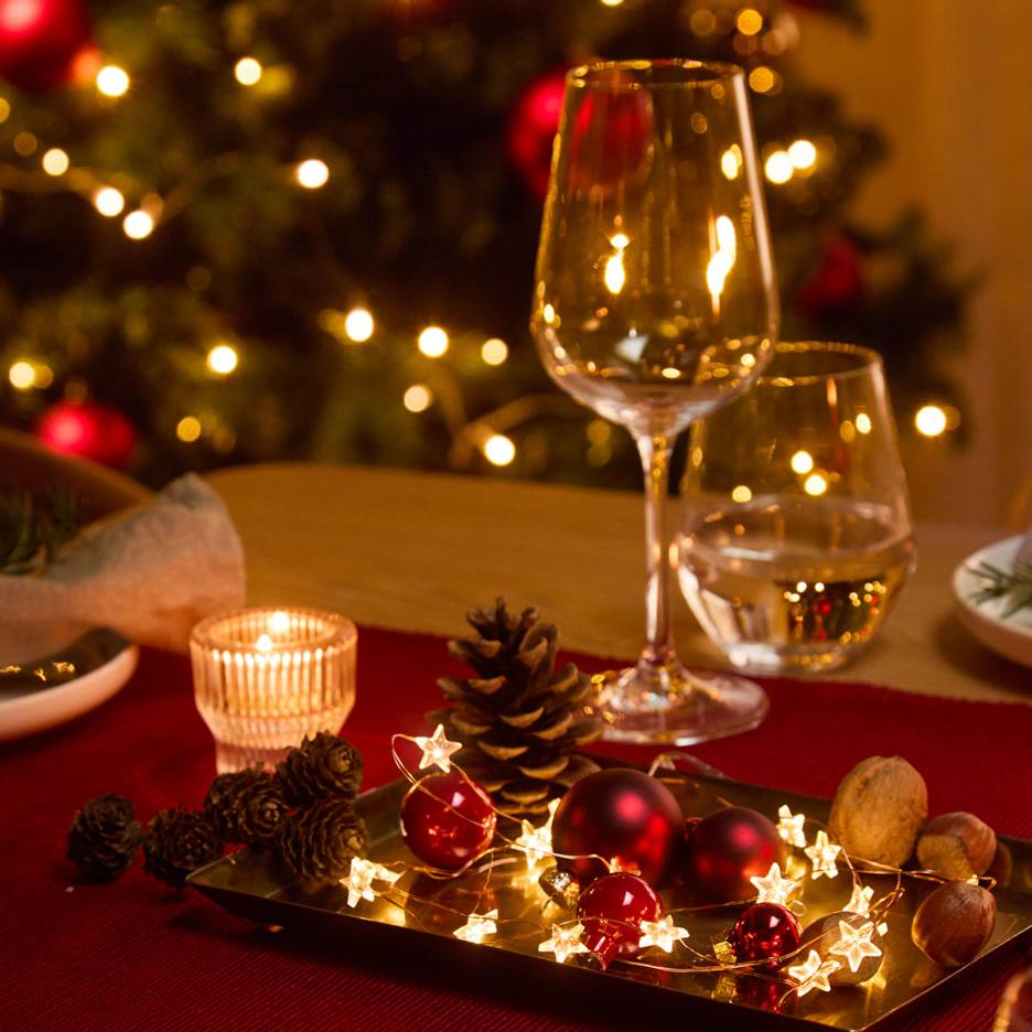 Christmas table decoration with glasses, candle, and string lights.
