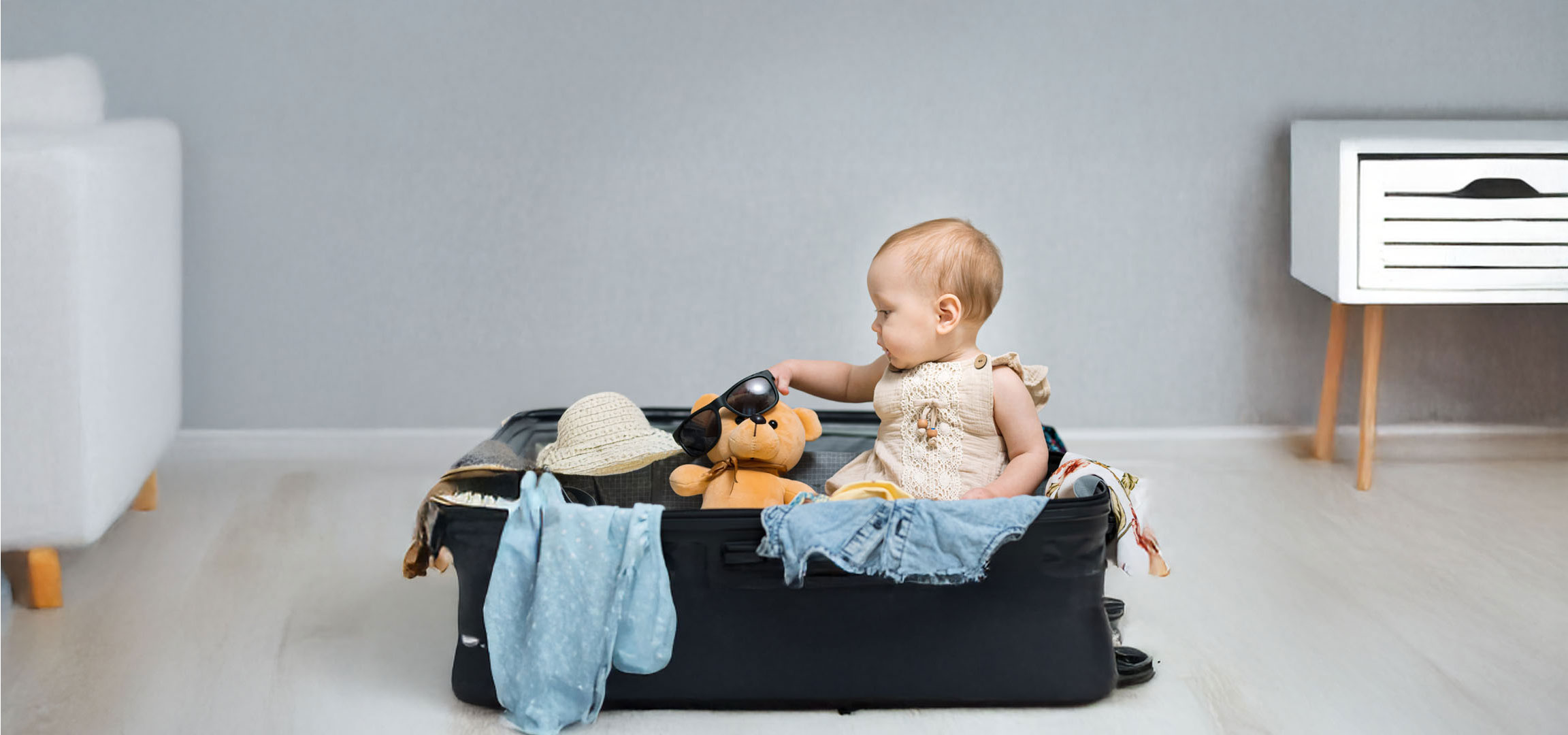 Baby packing clothes and a teddy bear into a suitcase.