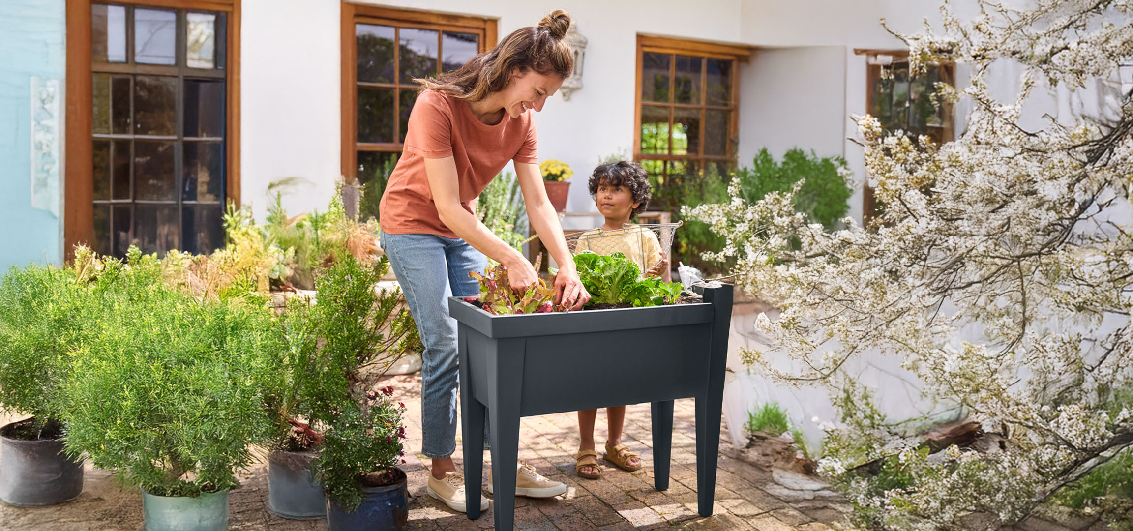 A mother and child planting vegetables in a dark grey raised garden bed.