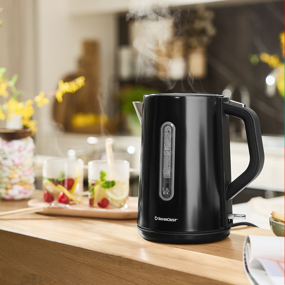 Steaming black SilverCrest kettle with refreshing drinks on a wooden counter.