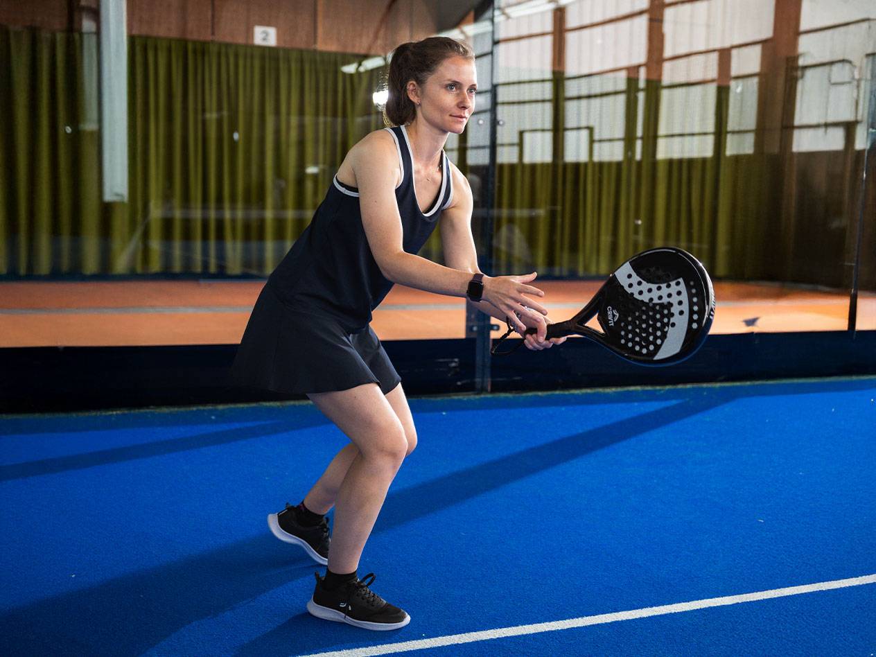 Lana Büttner in a black padel dress with a black padel racket on a blue court.
