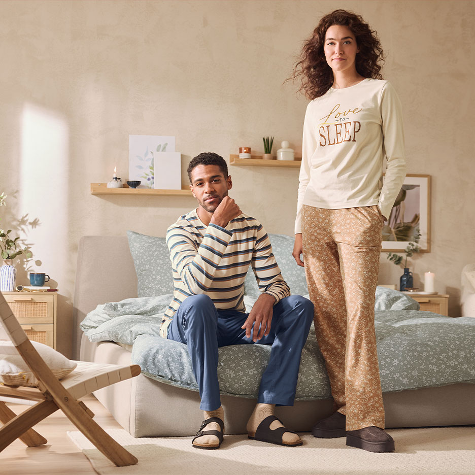 Couple in pajamas: man in striped top and blue pants, woman in 'Love to Sleep' top and patterned pants.