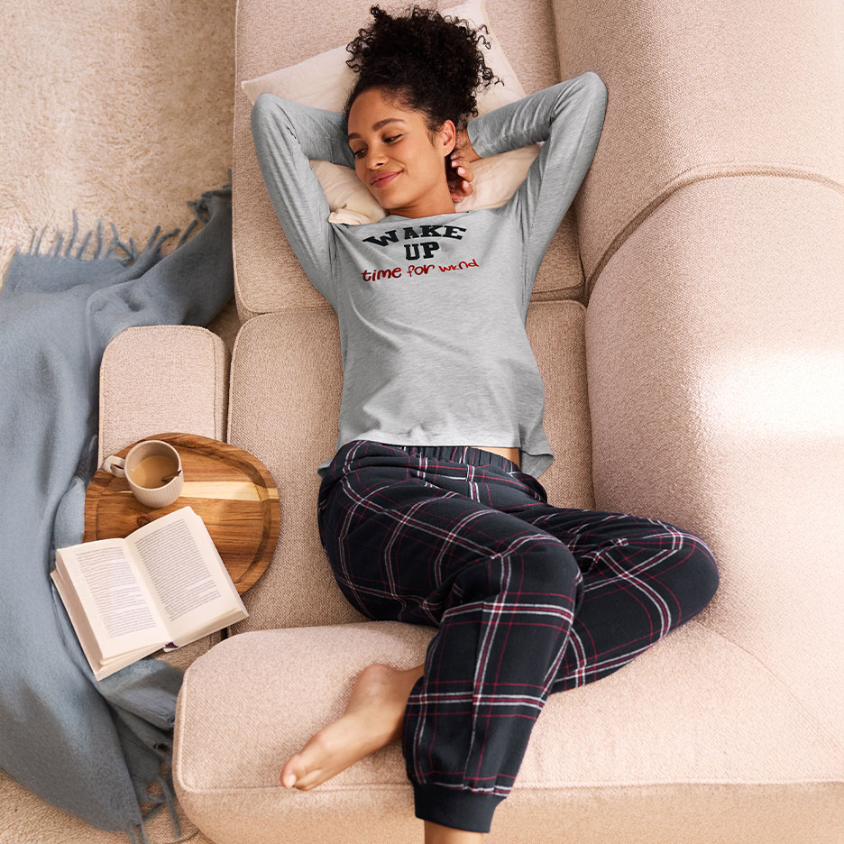 Woman in pajamas with 'WAKE UP time for wine' text relaxing on the sofa.