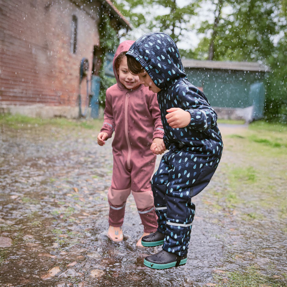 Two children in rain suits jumping in puddles.