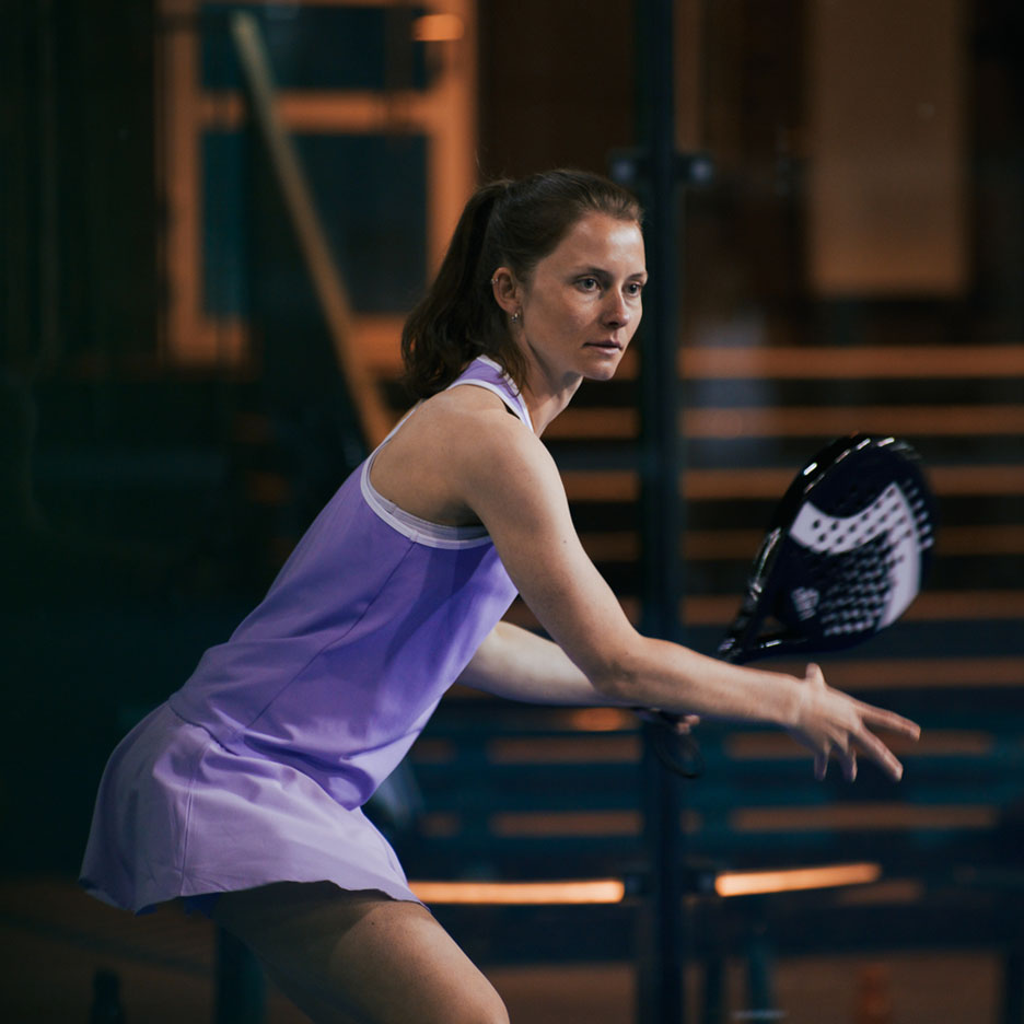 Woman playing padel in a purple dress.