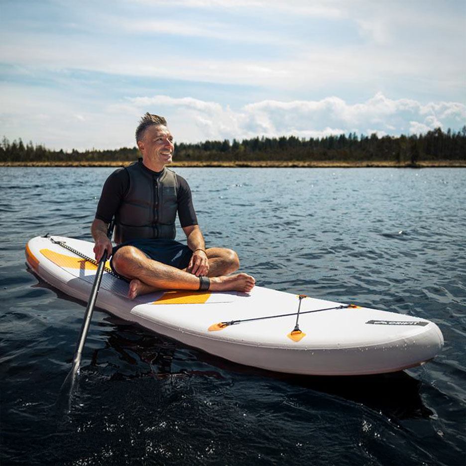 Man relaxing on a stand-up paddleboard on a lake.