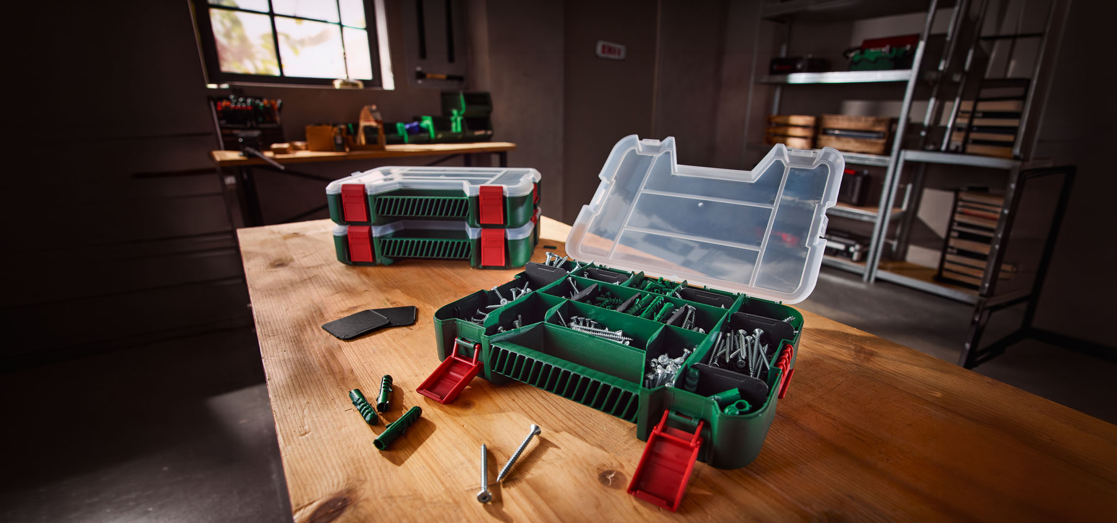 Open tool organizer with screws and wall plugs, and two closed organizers on a wooden bench.
