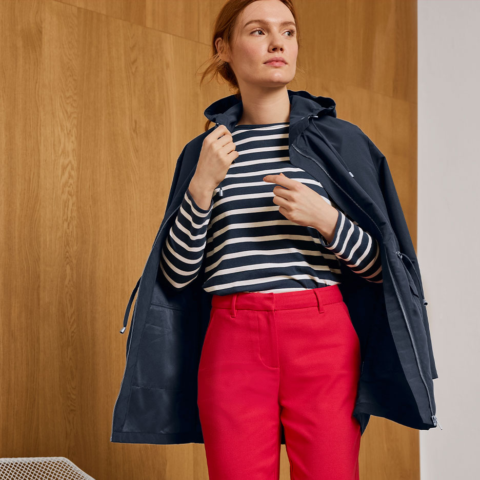 Woman in a navy striped top, red trousers, and a navy hooded jacket.