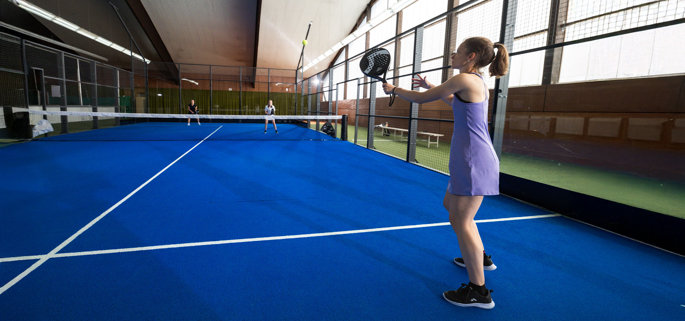 Lana Büttner playing padel on the court with a Crivit racket, yellow ball and other players.