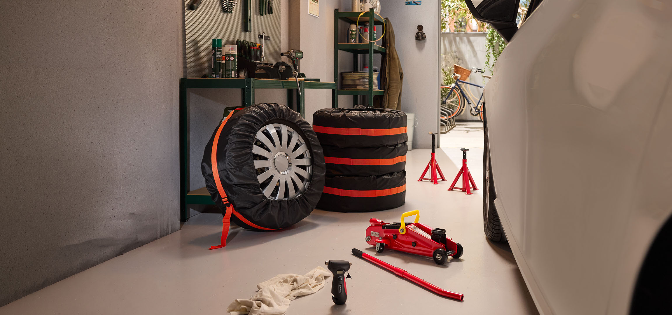 Winter tires stored in a garage with a hydraulic jack and jack stands.