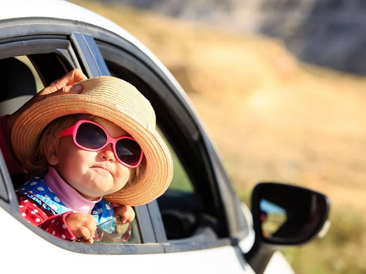 Toddler wearing a sunhat and sunglasses in a car.